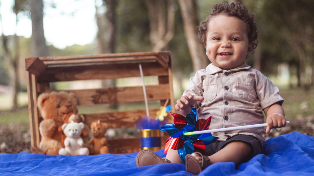 Little boy named Aidan sitting on a blue blanket with toys around him